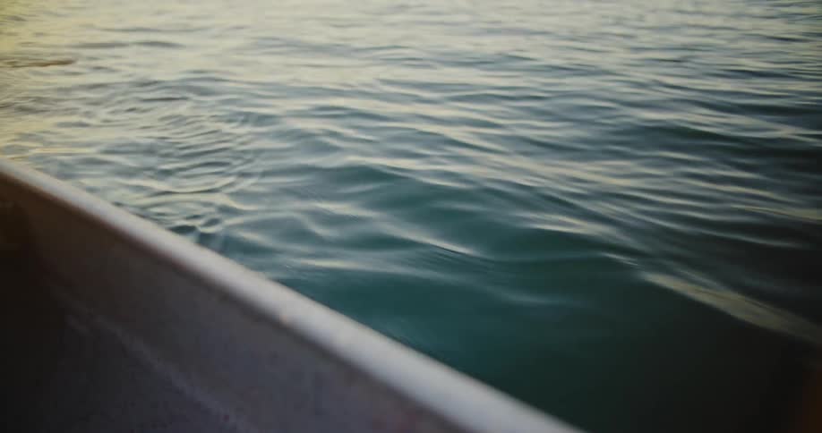 Dynamic view from inside a boats edge showing a persons hand repeatedly dipping a paddle with a yellow blade into the darkcolored water creating ripples