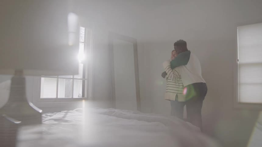 Couple hugs affectionately in a bedroom lit by natural light
