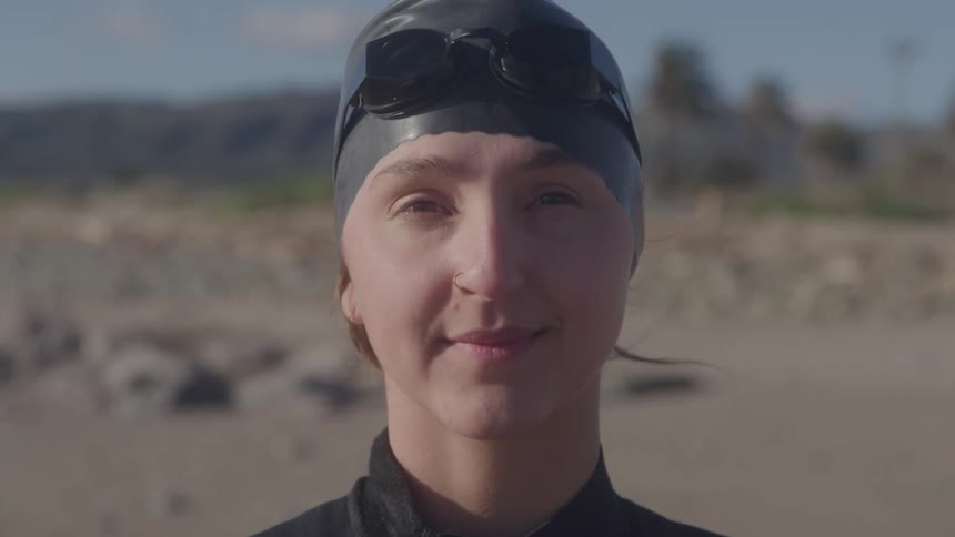 Woman wearing a swim cap and goggles smiles softly in an outdoor setting