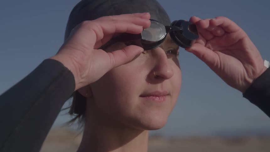 The face of a young woman putting swimming goggles on her eyes and she is wearing a black swimming cap