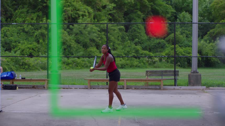 A female tennis player in a red top and black shorts practices her serve on an outdoor court