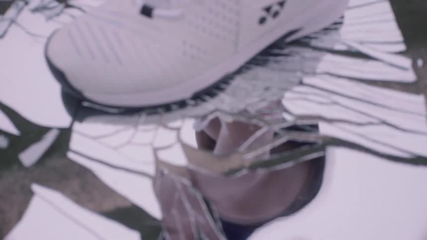 Woman with a tennis racket steps on a glass on the floor and cracks it