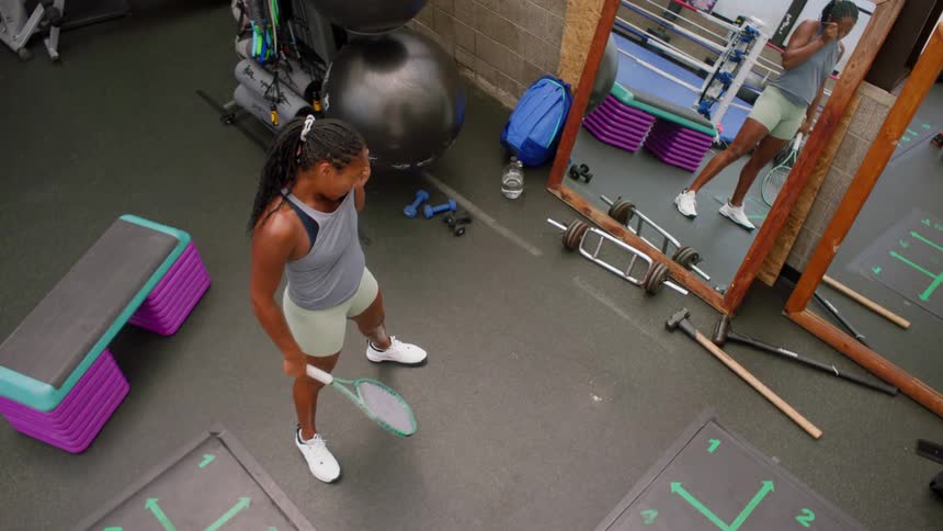 A woman intensely practices tennis swings in a gym