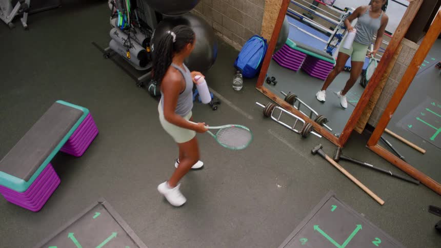 Woman in athletic wear drinks water while practicing tennis