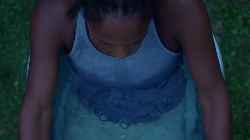 A black female sits into a metal tub full of water on grass