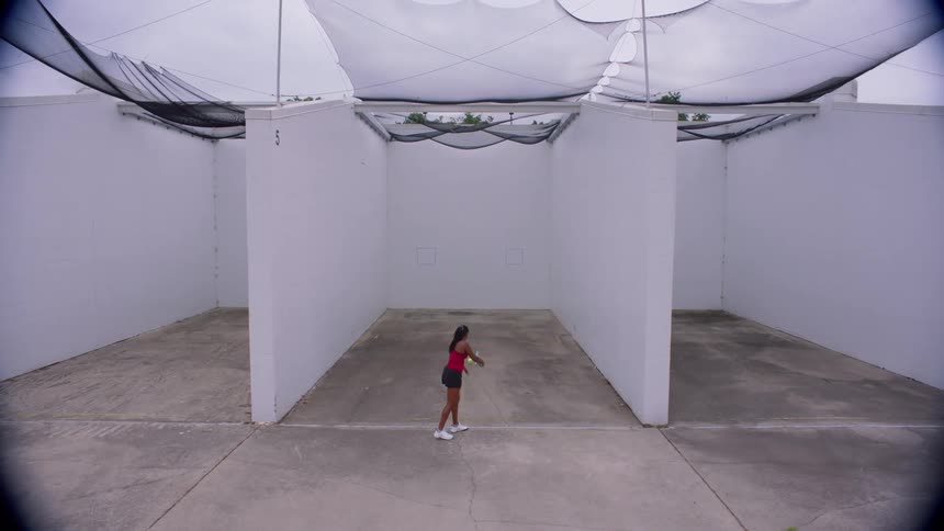 Person playing tennis on a court surrounded by white walls