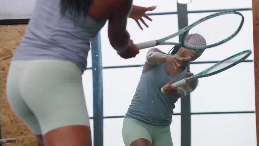 A woman holding a tennis racket practices arm movements in a mirror