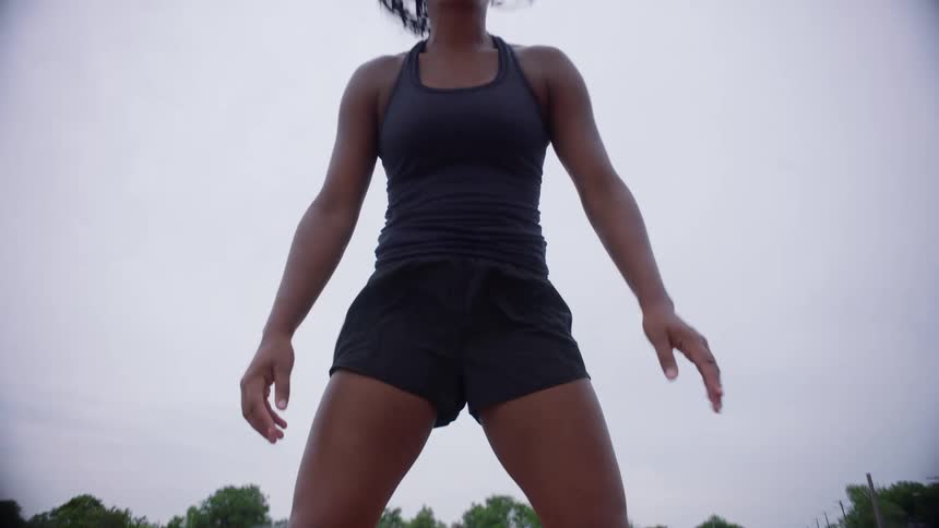 A black female runner in white trainers stretches on the red track lane fingertips to ground poised and determined