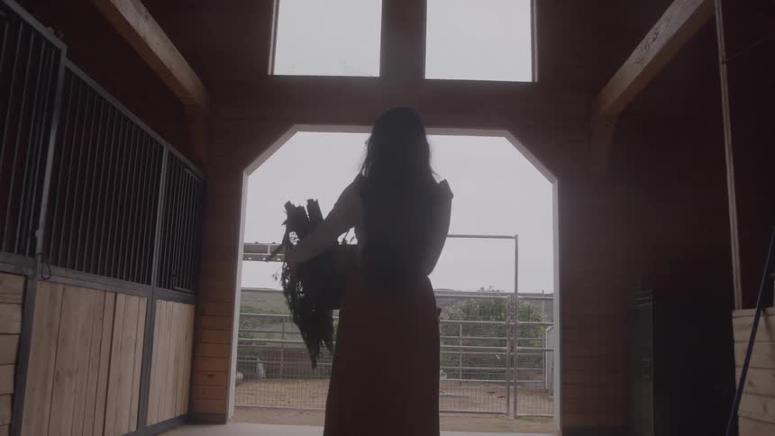 Woman carries plants while entering a barn lit by natural light