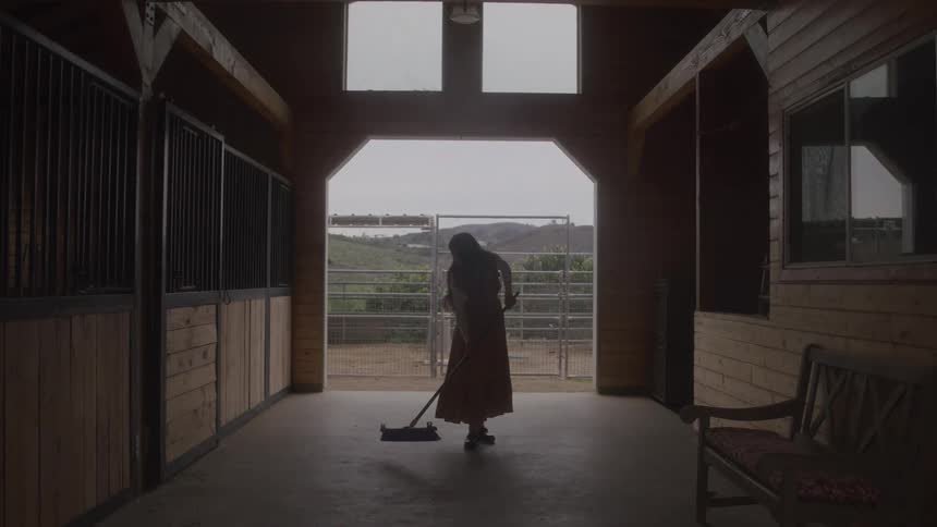 Woman sweeping the floor of a wooden stable