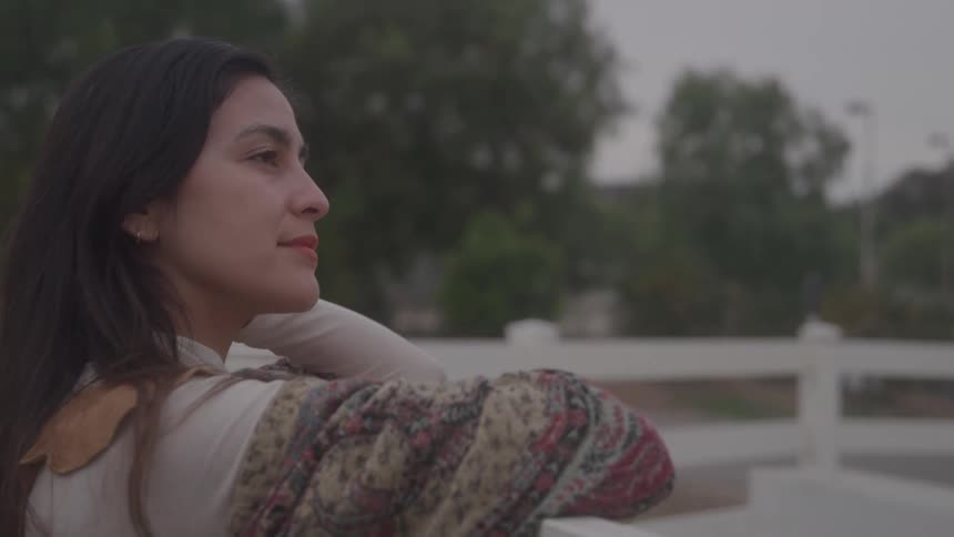 Woman gazes into the distance with a calm expression resting her hand on her neck outdoors