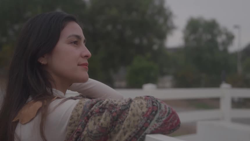 A woman leans on a fence gazing thoughtfully into the distance outdoors
