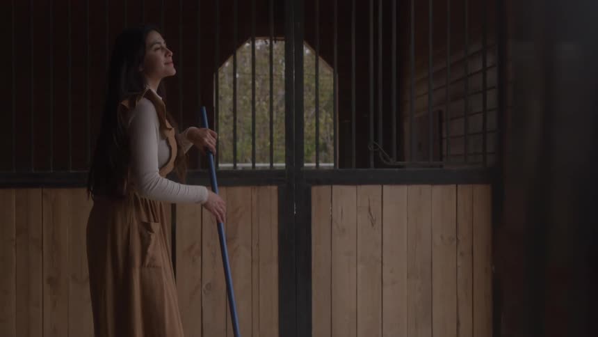 Woman holds a handle and smiles softly while looking at the landscape outside the stable