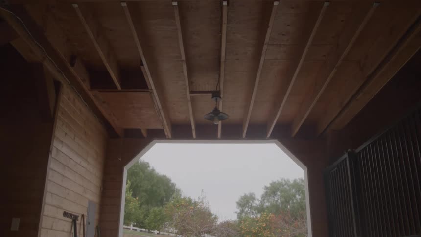 An open barn doorway framed by wooden beams onto a cloudy outdoors