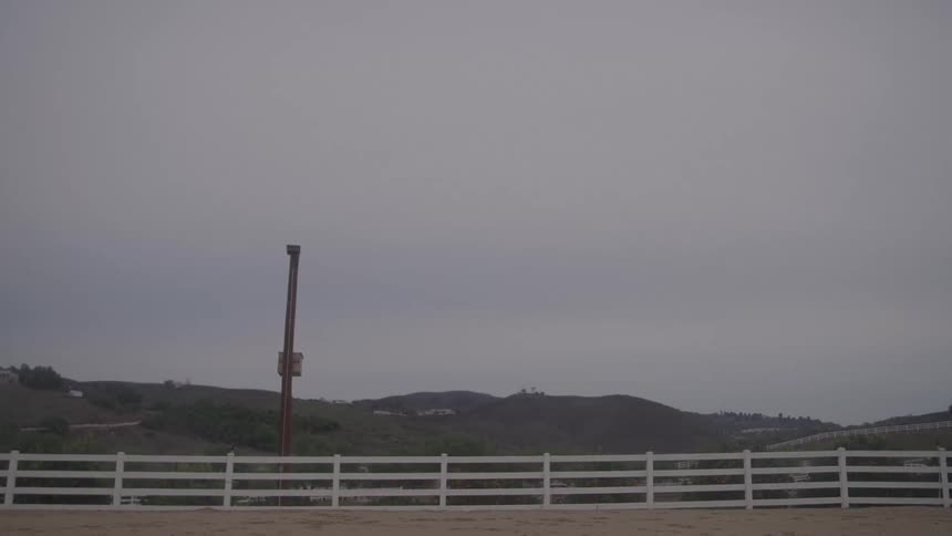 A quiet rural landscape with a white fence hills and a cloudy sky