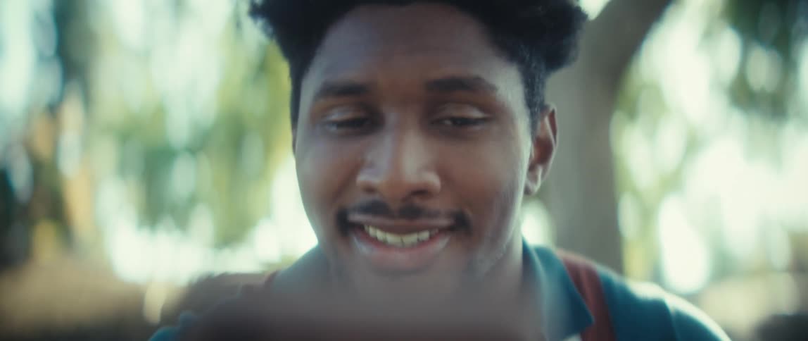 Close up of a young black man conversing with a caller on an electronic device while sitting outdoors during daytime