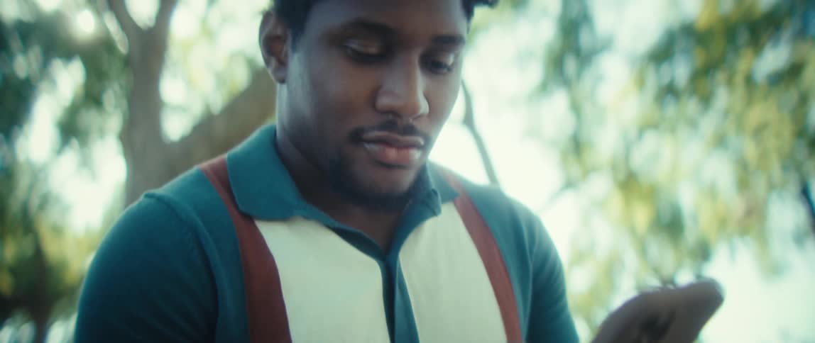 A man in a teal collared shirt studies his phone with a calm happy expression