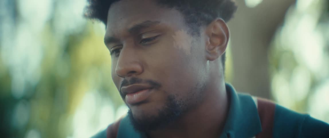 A mans face speaking to a smartphone positioned outdoors with his head partially obscured by a bright light source against a blurred green background