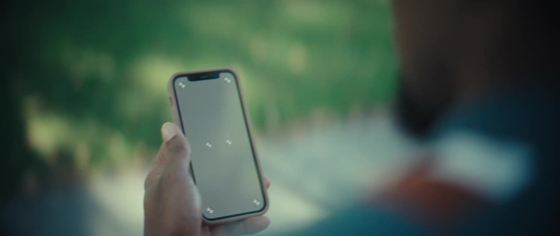 A persons hand holding a cell phone with a gray screen in an outdoor environment