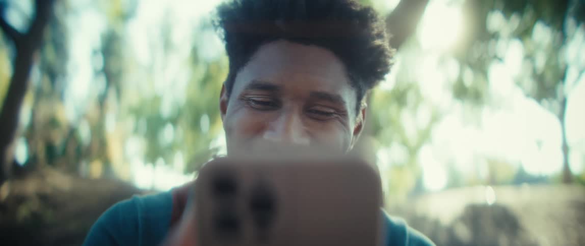 Person looks at phone screen in outdoor setting with sunlight filtering through trees