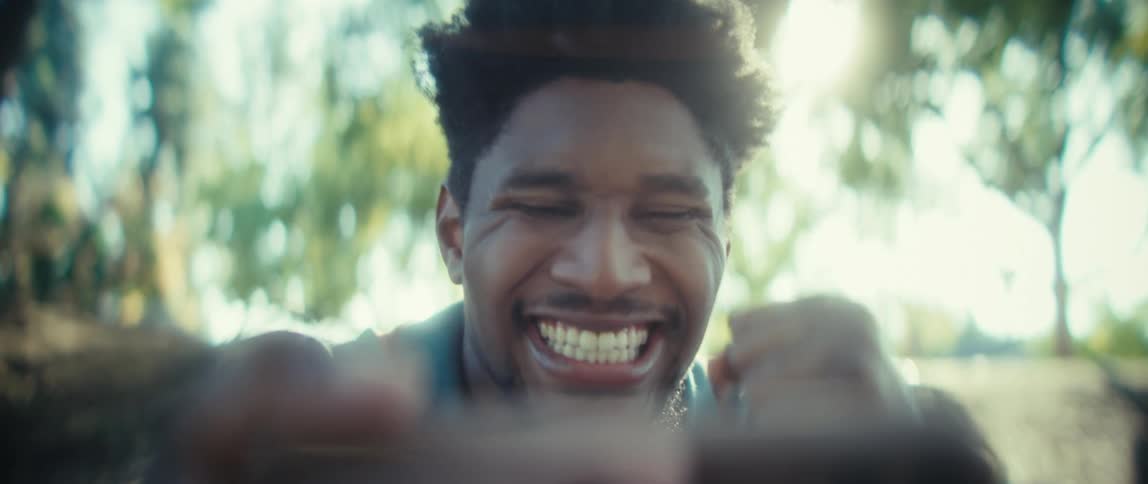 A man laughs excitedly during a video call outdoors in the sunlight