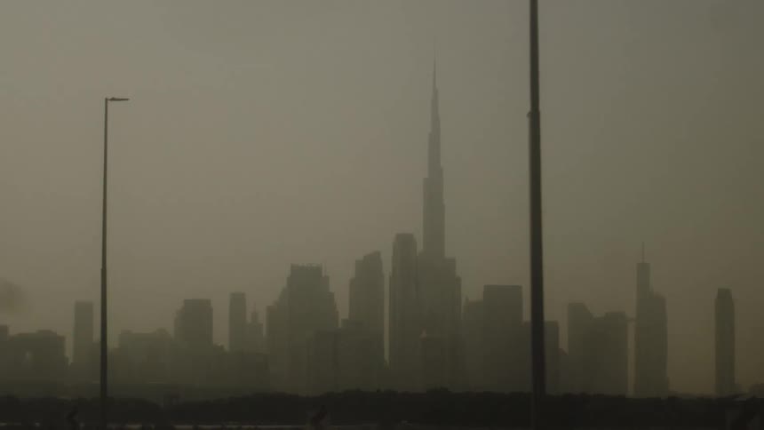 A city skyline stretches into view at sunset with streetlights lining the road as a blanket of fog softens the atmosphere