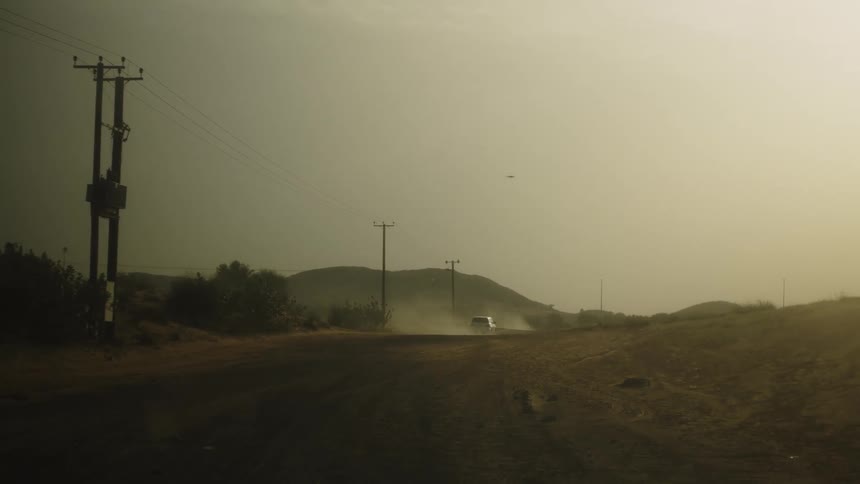 Cars raising dust on a rural road at sunset