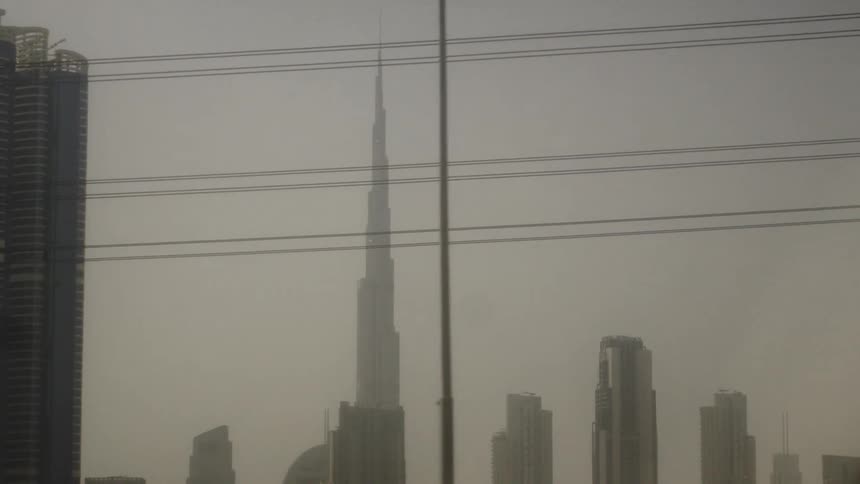 A view of a dense cityscape is shrouded in a thick dusty haze with the burj khalifa towering in the center and several power lines running horizontally across the foreground