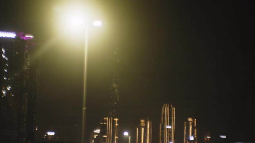 Bright streetlight illuminates the nighttime cityscape with skyscrapers in the background