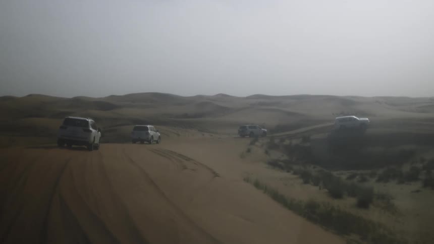 Multiple cars driven together along a sandy road in a desert area during daytime