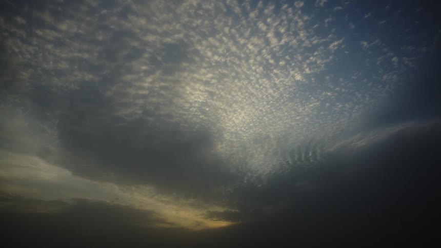 A timelapse video shows an expanse of patterned clouds filling the sky darkening as the daylight fades into night and the sun disappears below the frame