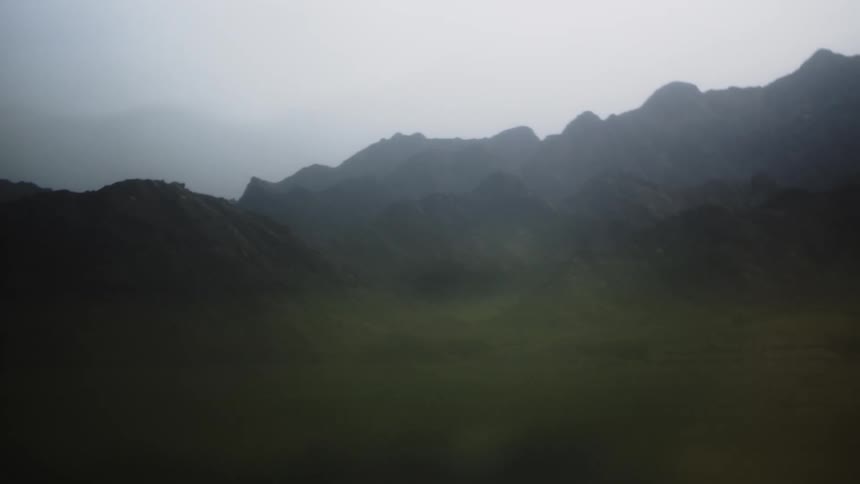 Misty mountains rise over a hazy green landscape