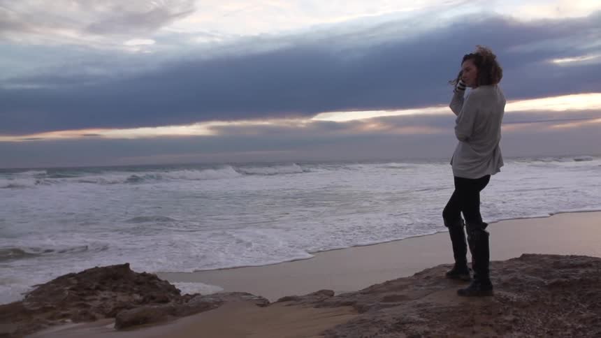 Woman stands on some rocks by the shore