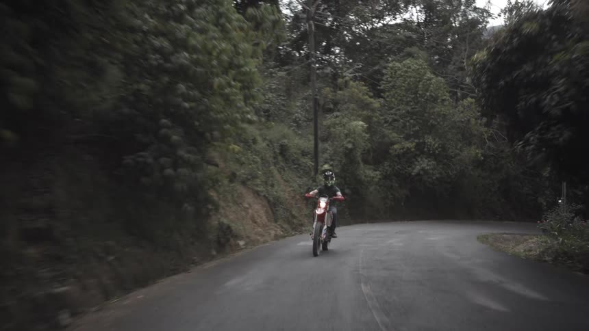 Motorcyclist rides along a narrow road surrounded by vegetation and mountains