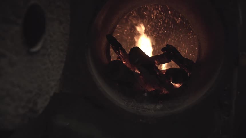 Closeup logs crackle and spit sparks as bright flames roar in a circular fireplace