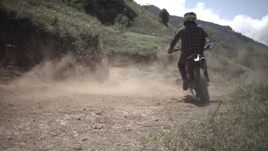 Motorcyclist kicking up dust while riding on a dirt trail