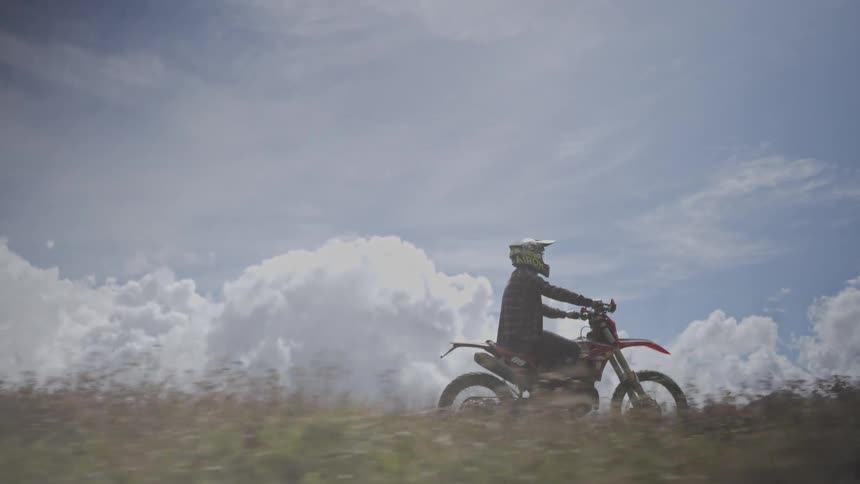 A person riding on a dirt bike on a bummy hilly path under billowing clouds