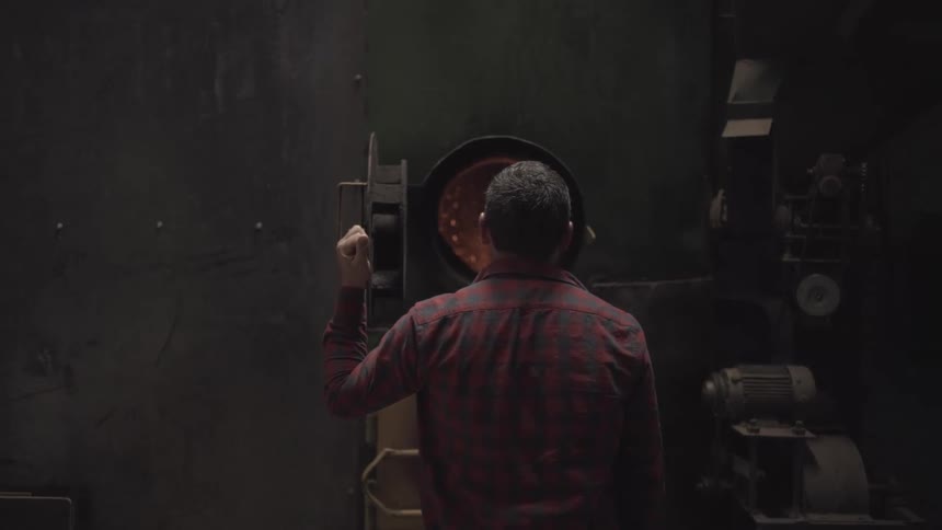 A man closes a furnace door in factory and walks away