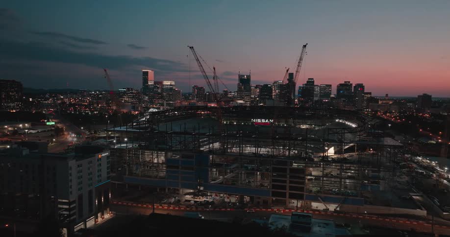 Construction site surrounded by cranes with the illuminated city in the background