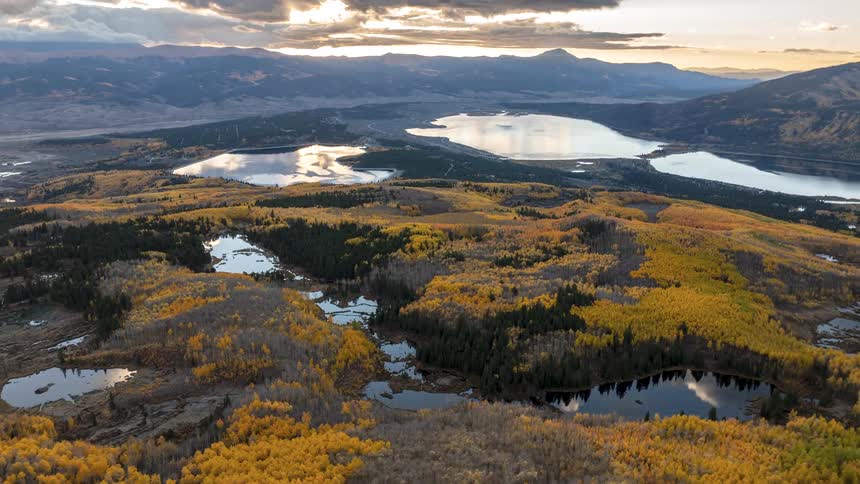 Forest with autumn tones stretches toward lakes surrounded by mountains at sunset