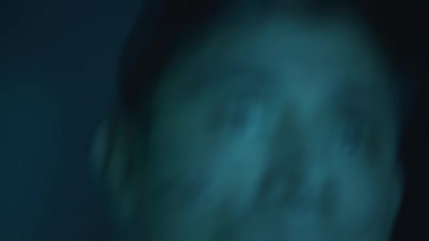 A young man stands outdoors at night in the dark looking scared and afraid