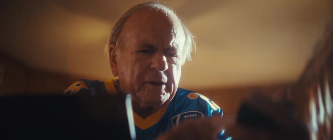 An elderly man sits in his living room scrolling through his phone