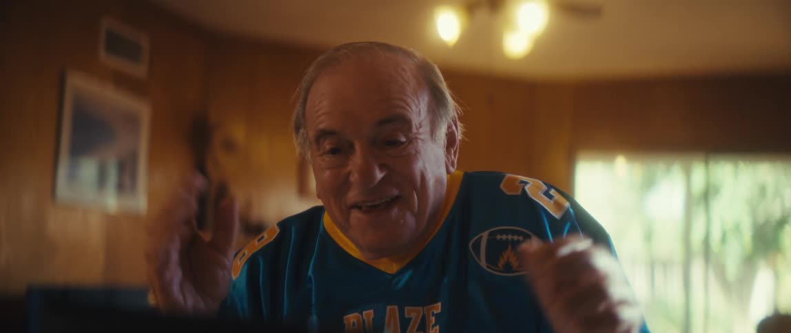 Elderly man in a sports shirt cheering while watching on a tablet