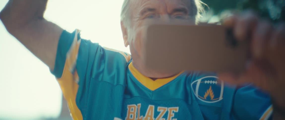 Elderly man outdoors in a vibrant and happy manner raising his arm while watching on a smartphone