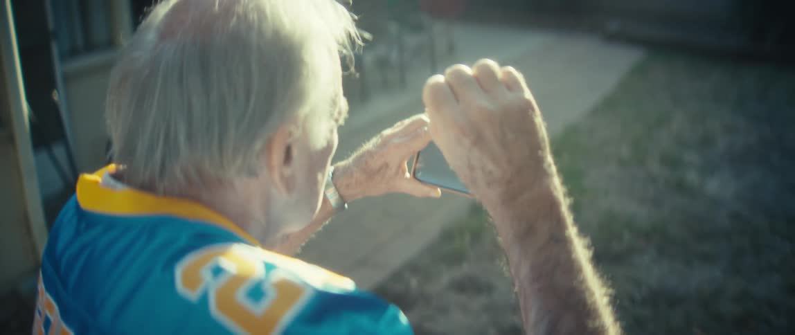 Elderly man in an outdoor backyard cheering while watching on a smartphone