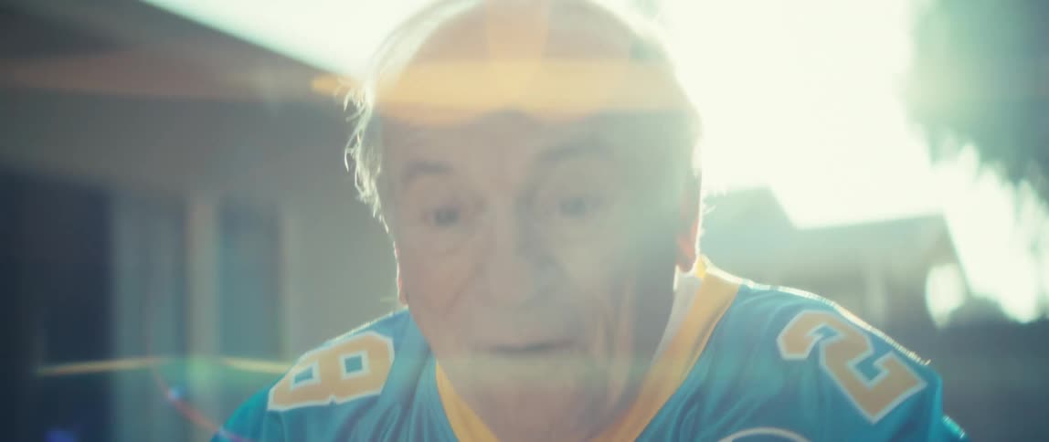 Elderly man in a backyard holding a smartphone and celebrating happily