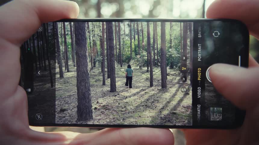 Pair of hands using an iphone and taking a picture of a person walking in the forest