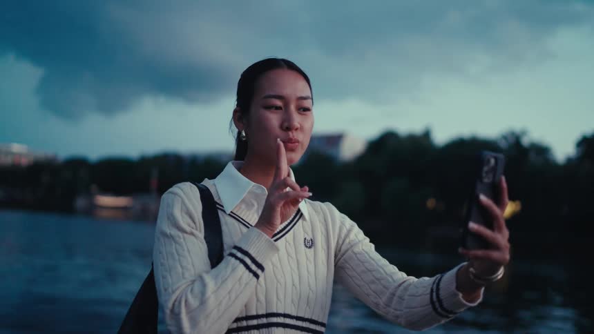 A woman by the waterfront takes a selfie flashing a peace sign looking relaxed