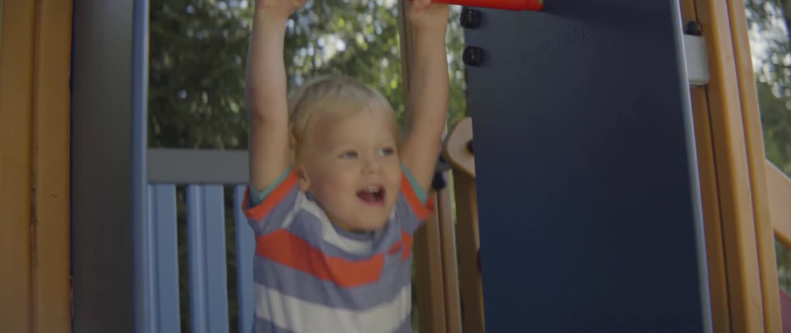 oung toddler boy smiling and laughing while playing on a colorful outdoor slide set.