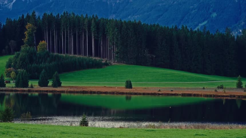 A small lake is by the forest and mountains